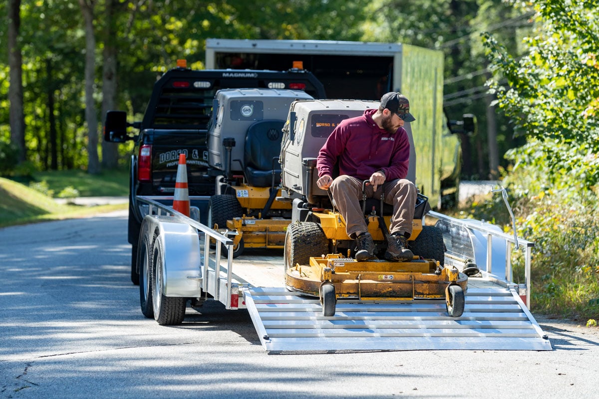 Driving a lawnmower off an open aluminum utility landscape trailer