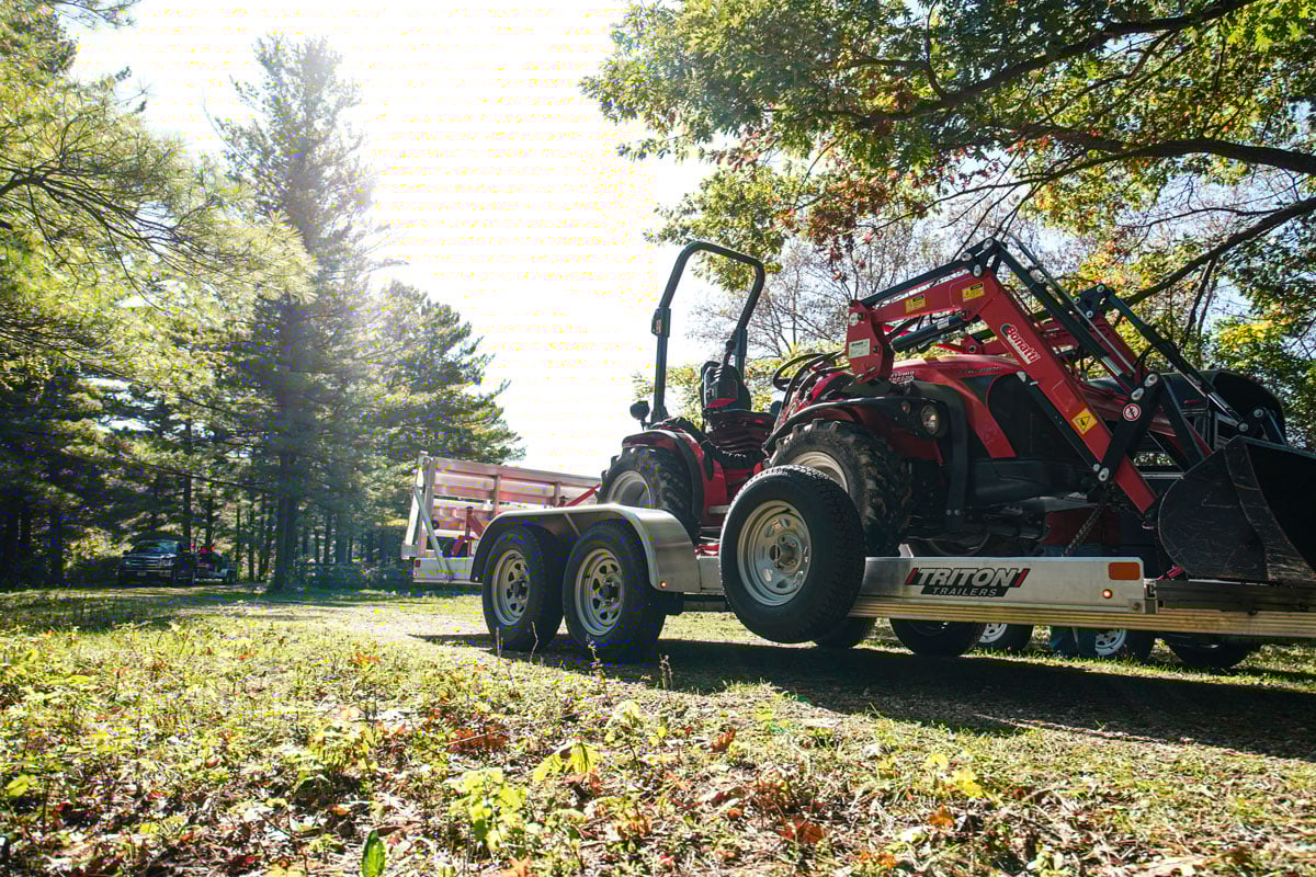 Red tractor parked on a heavy-duty ALCOM aluminum utility trailer