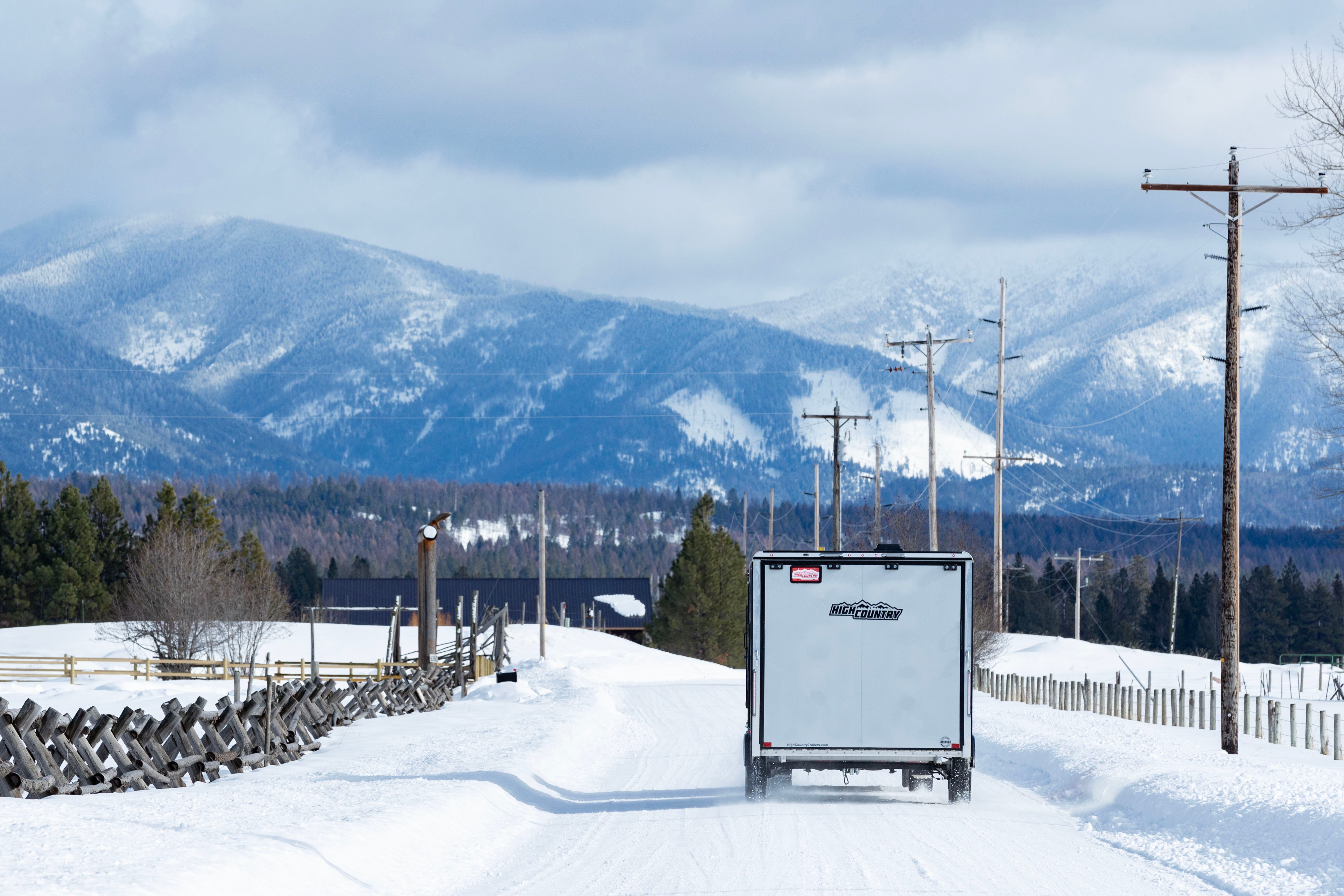 High Country All Sport Elevation Series enclosed aluminum snowmobile trailer on a snowy road towards distant mountains