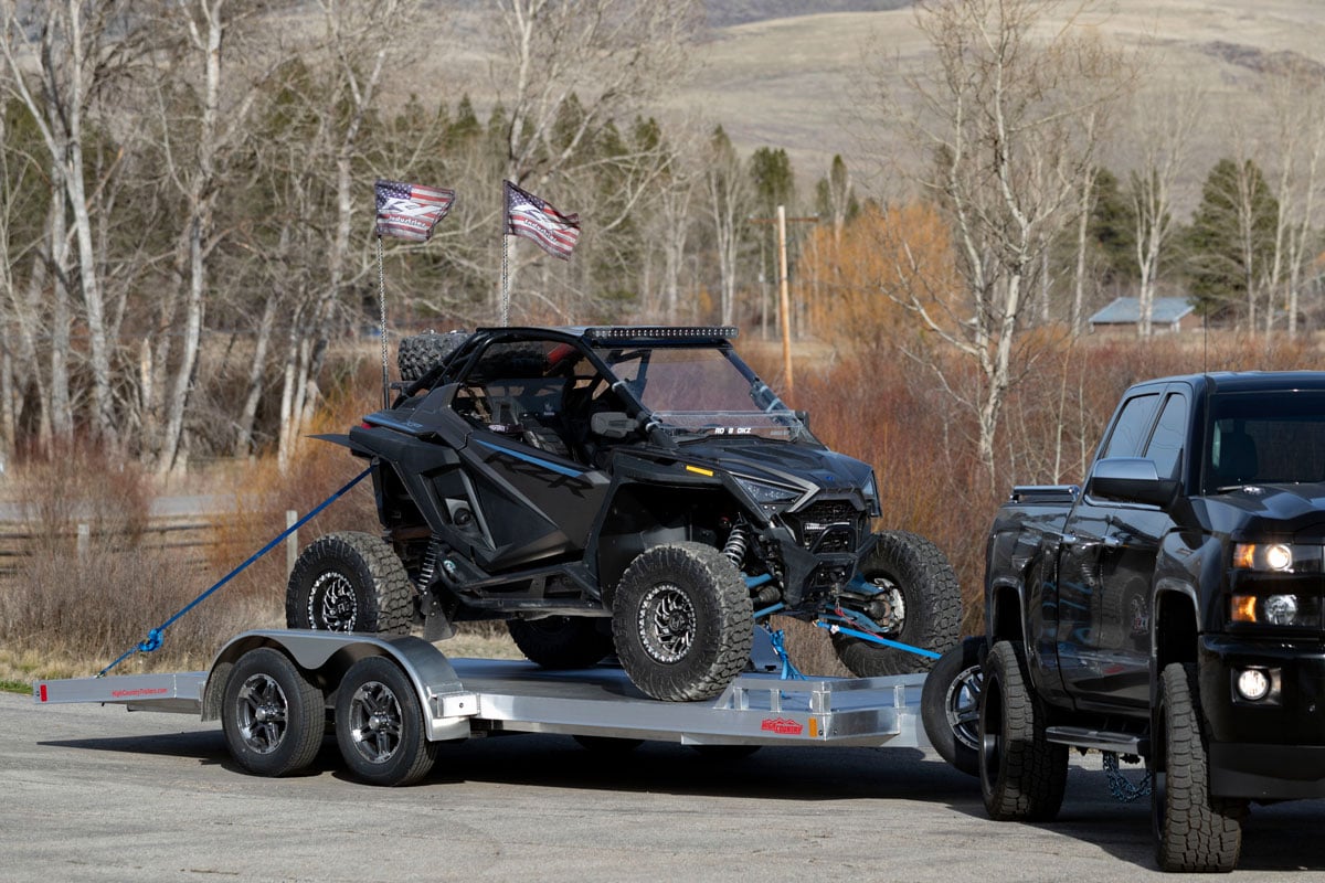 Open aluminum car hauler hitched to a Jeep hauling a UTV