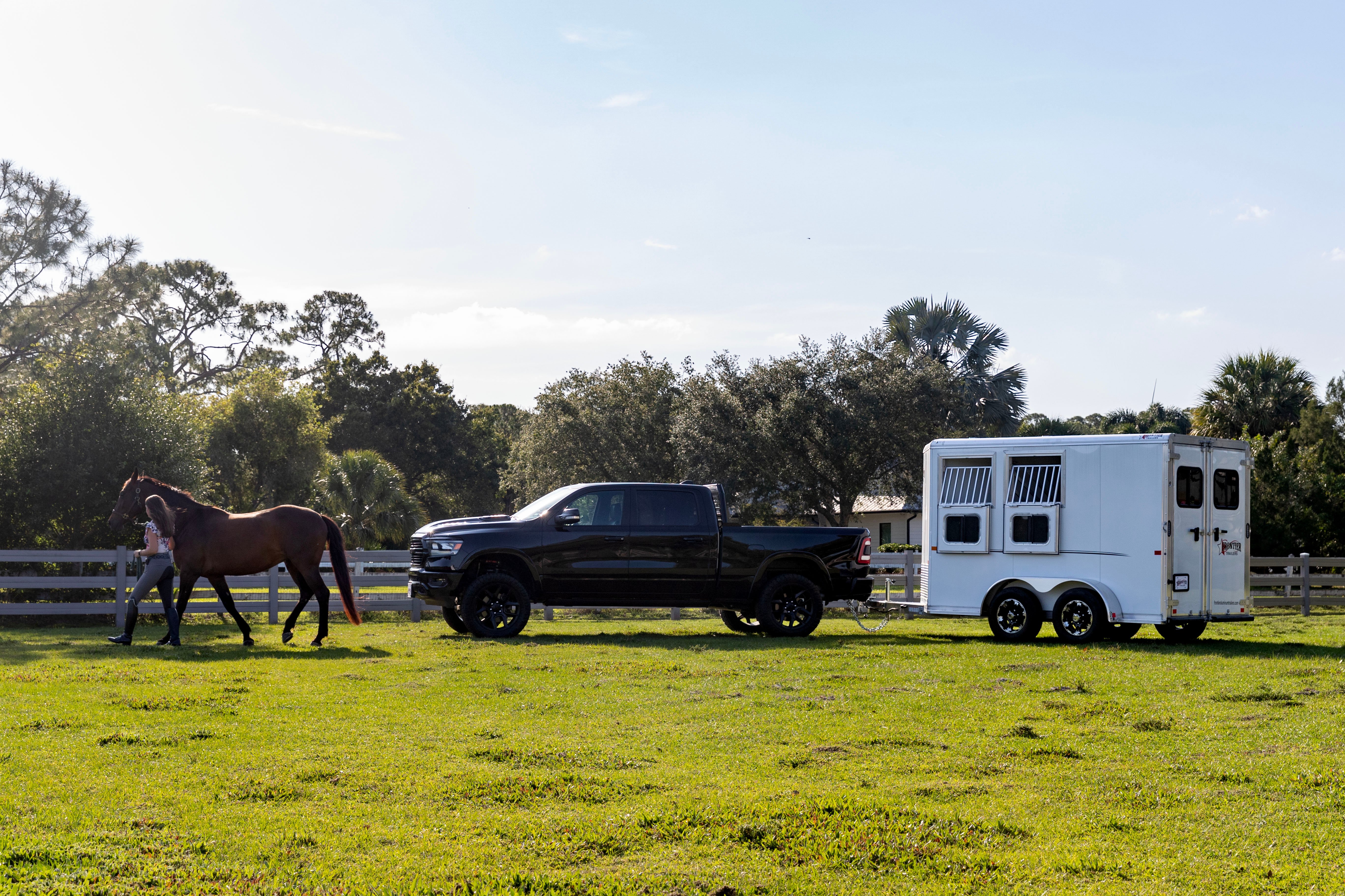 Woman leading a horse in a paddock near a white Frontier aluminum trailer and black pickup truck