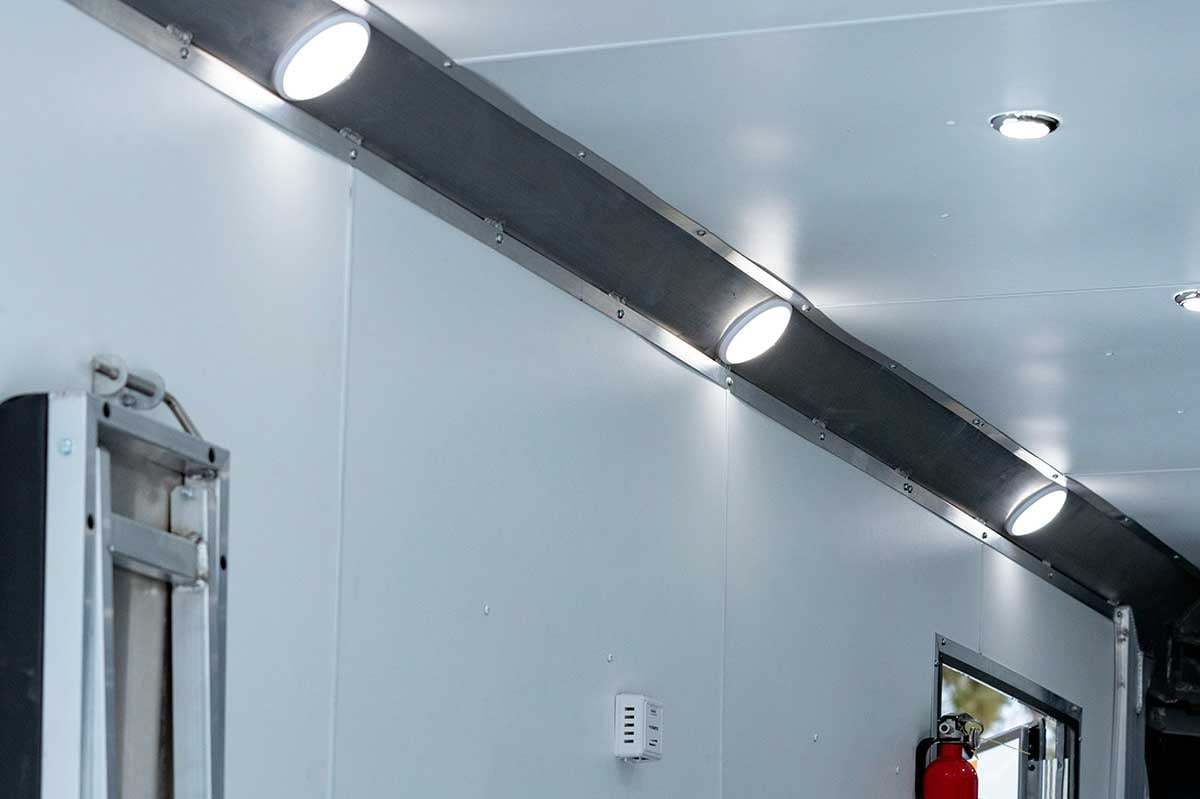 Lights installed inside the enclosed trailer; fire extinguisher and bench also installed; side access door open