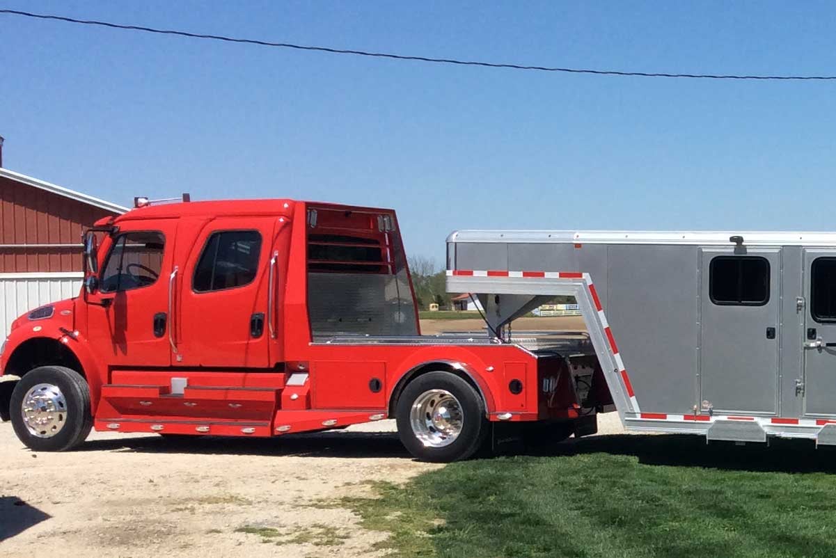 Red heavy duty truck towing a silver grey gooseneck trailer with side doors and windows