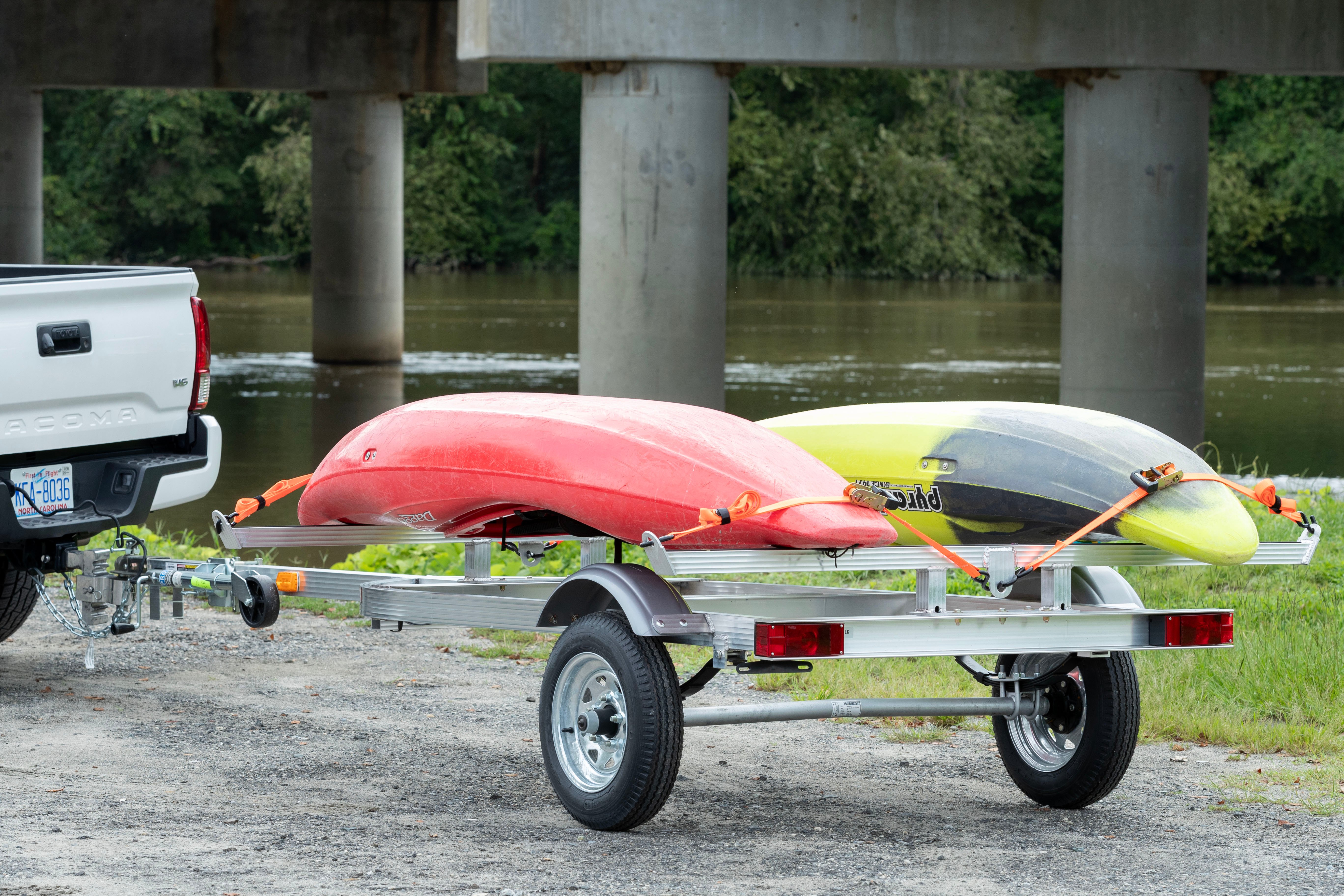 A Triton kayak trailer with 2 kayaks secured to its all aluminum frame parked near the water