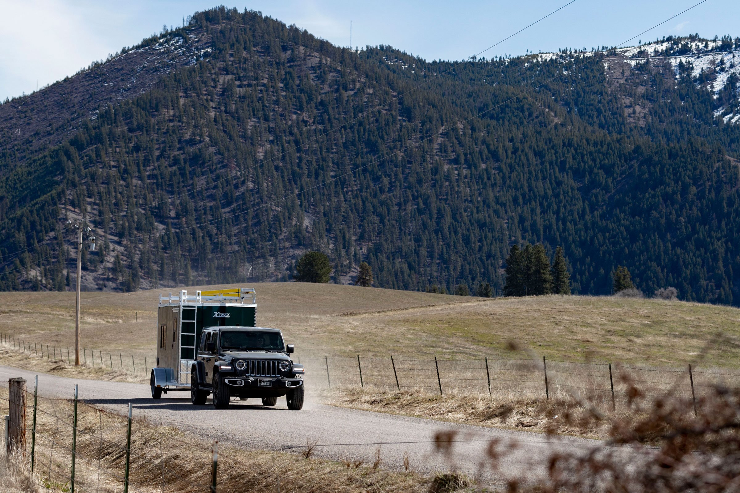 Jeep towing a green Ultimate Contractor Package trailer on a dirt road near mountains