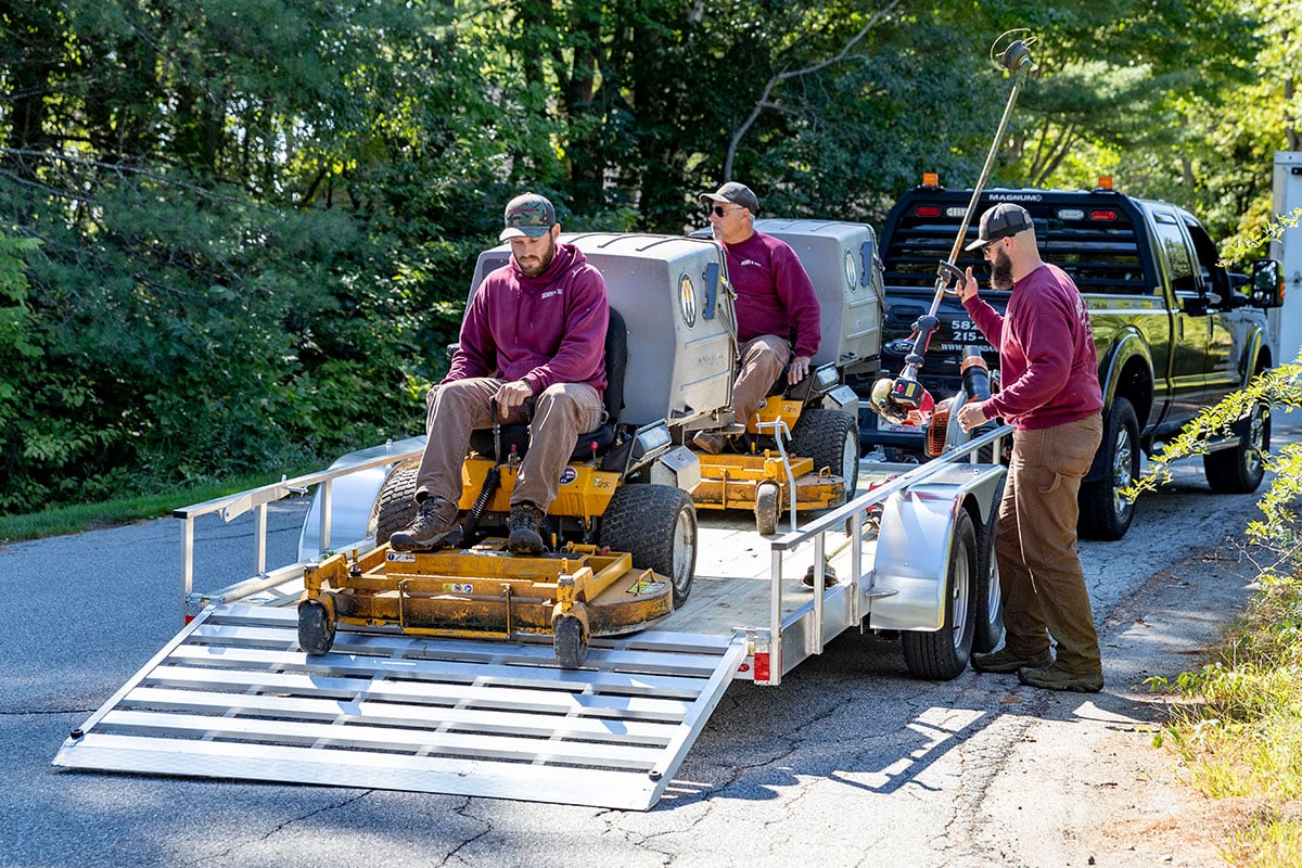 Unloading lawnmowers from an open wood deck utility landscape trailer by ALCOM