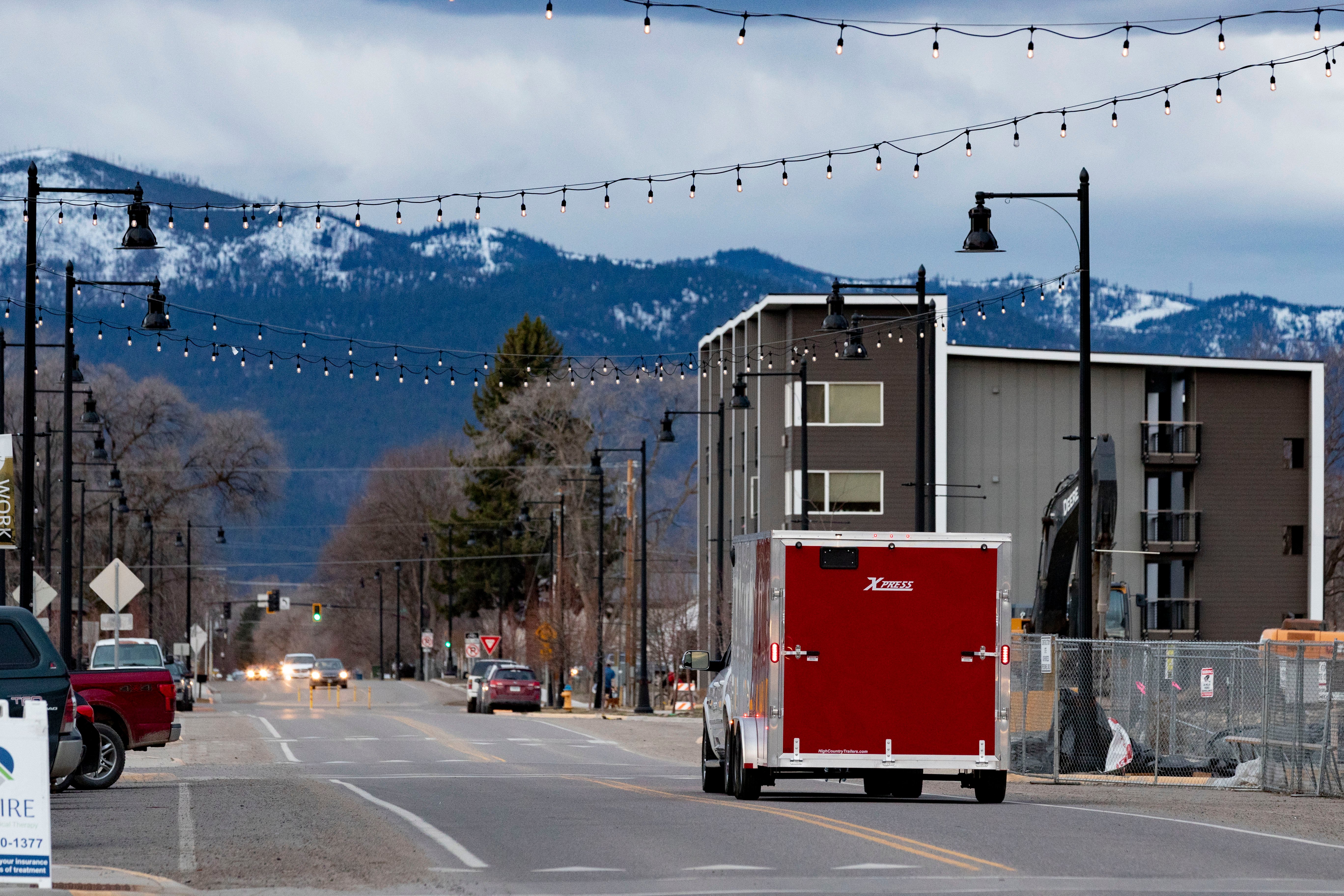 A red ALCOM enclosed cargo trailer towed through a Montana town with mountains in the background