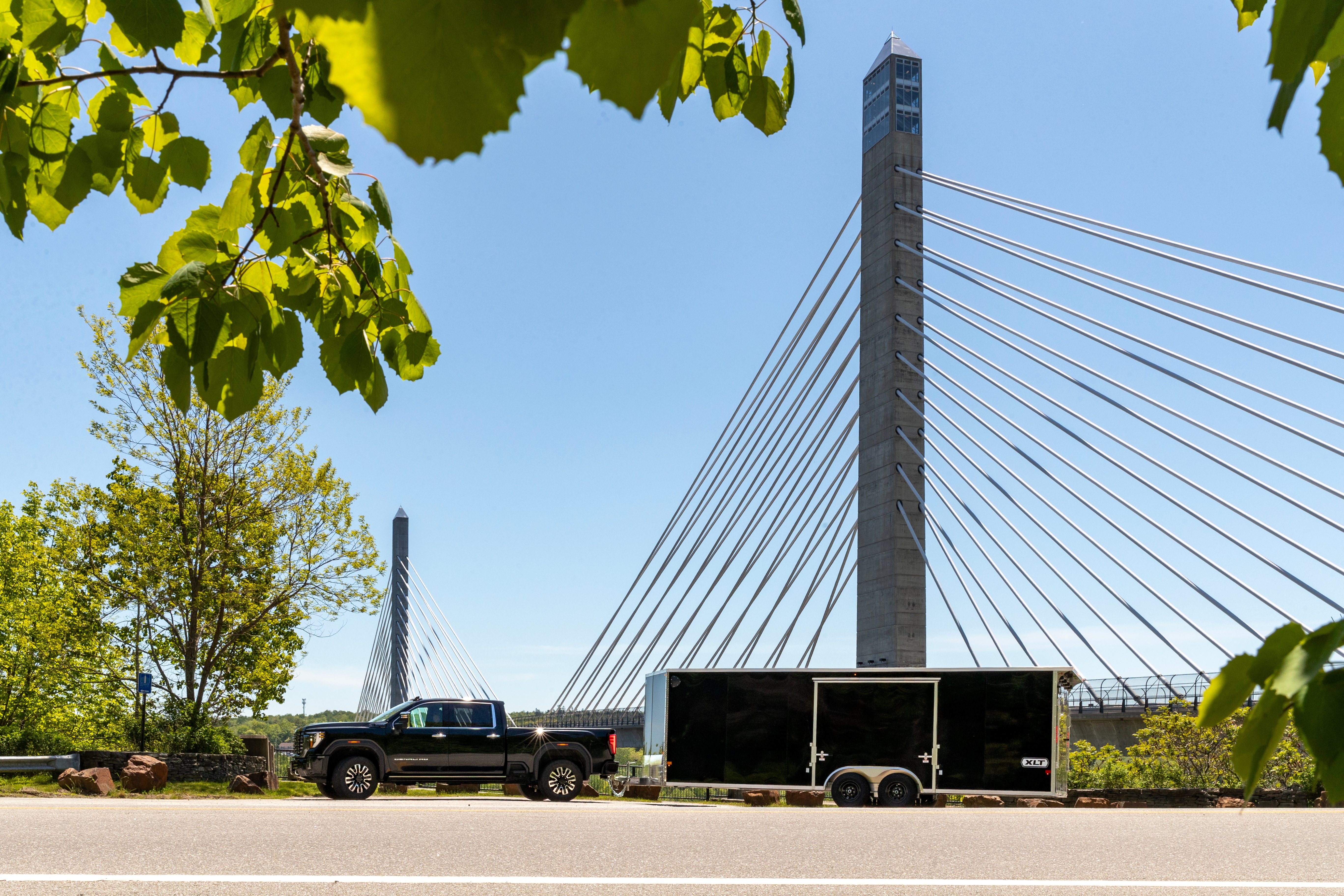 Black pickup and XLT Pro Series car hauler parked in front of a tall bridge in Maine on a sunny summer day