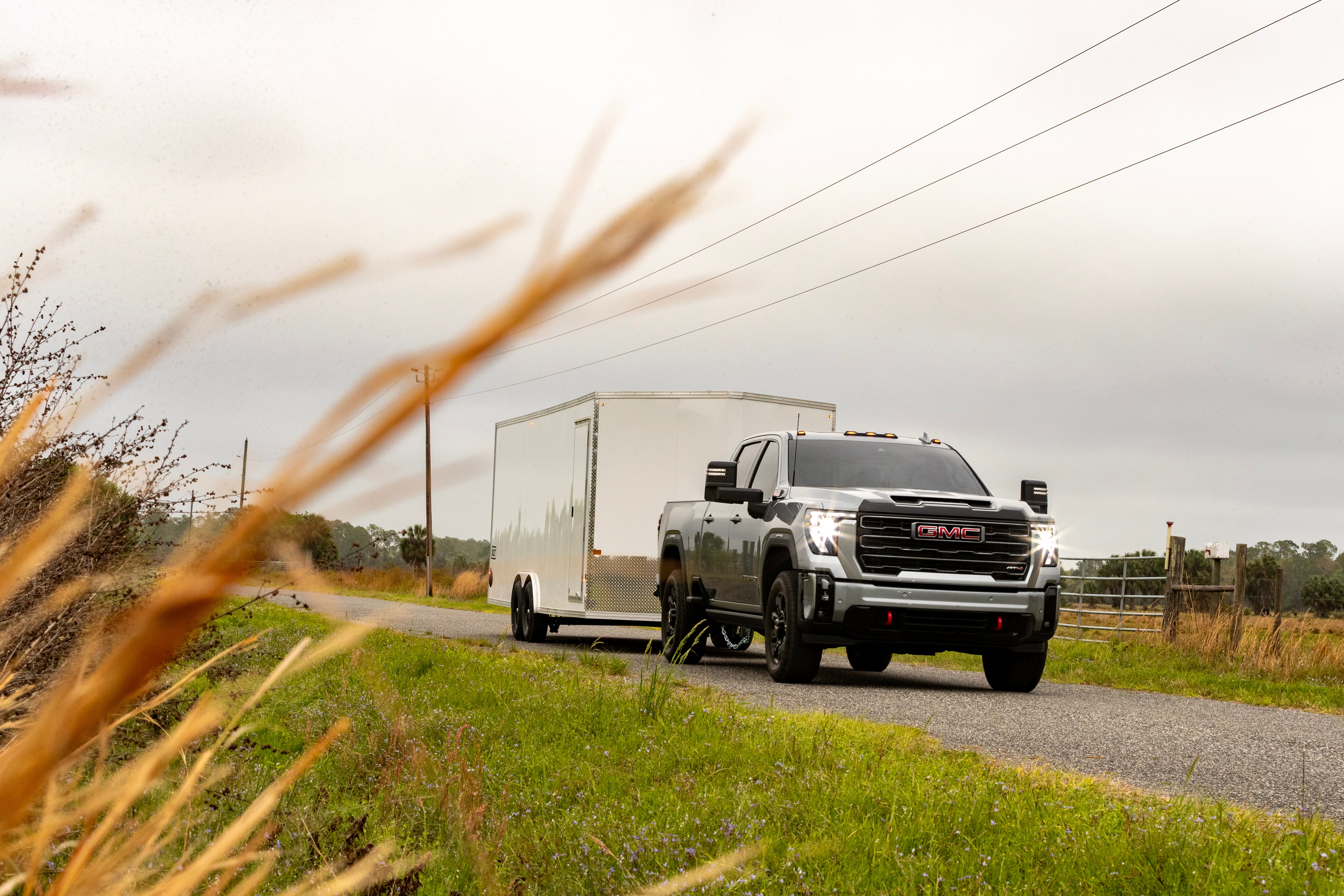 An enclosed aluminum car hauler towed on a farm road by a pickup truck