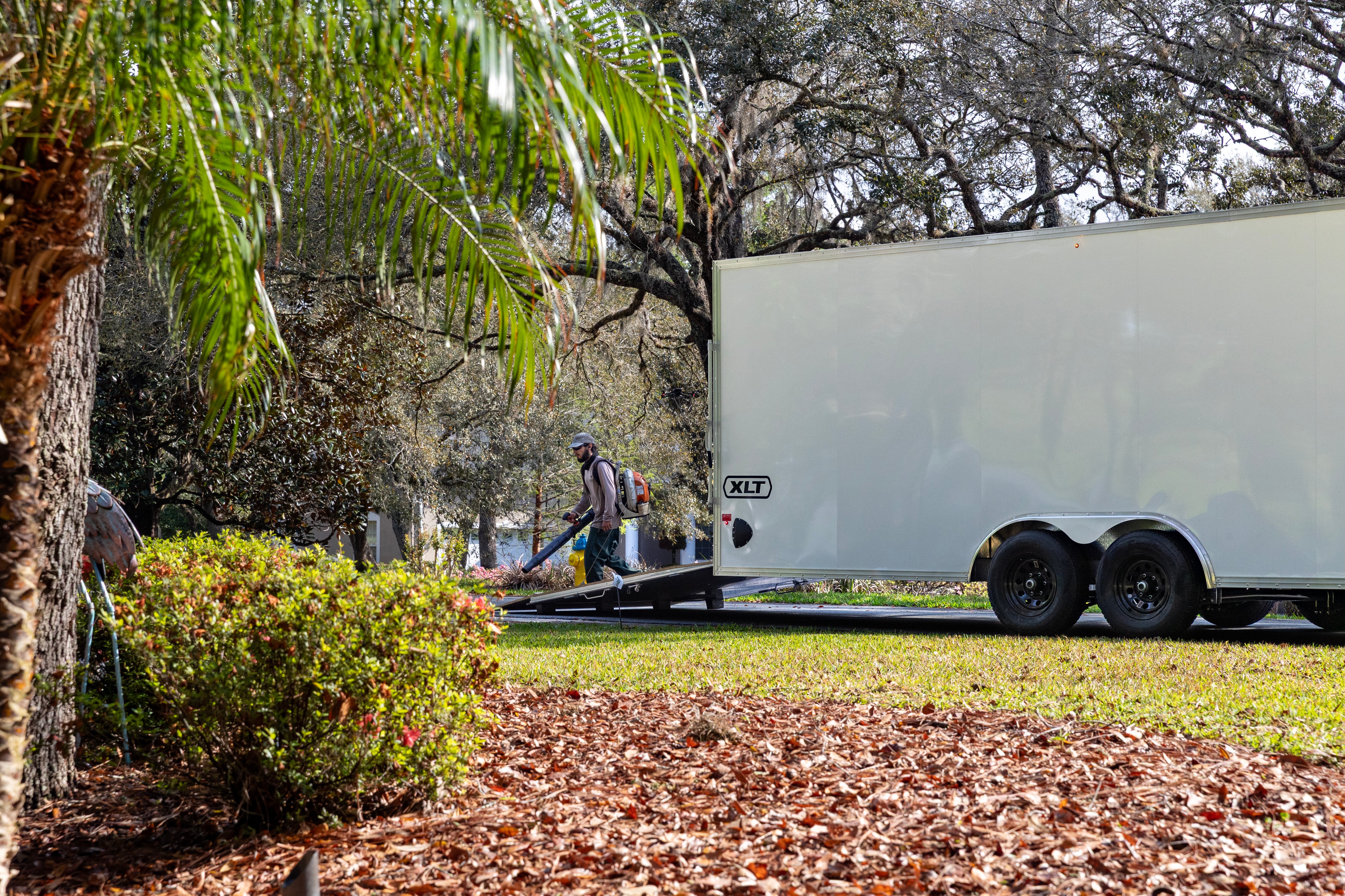 An enclosed XLT Pro Series car hauler parked with a landscaper working in the. yard