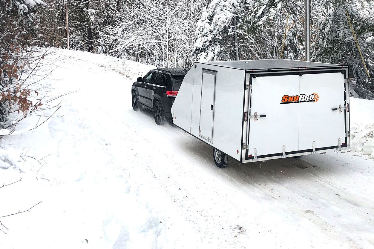 Aluminum Crossover snow trailer towed by an SUV on a snowy road
