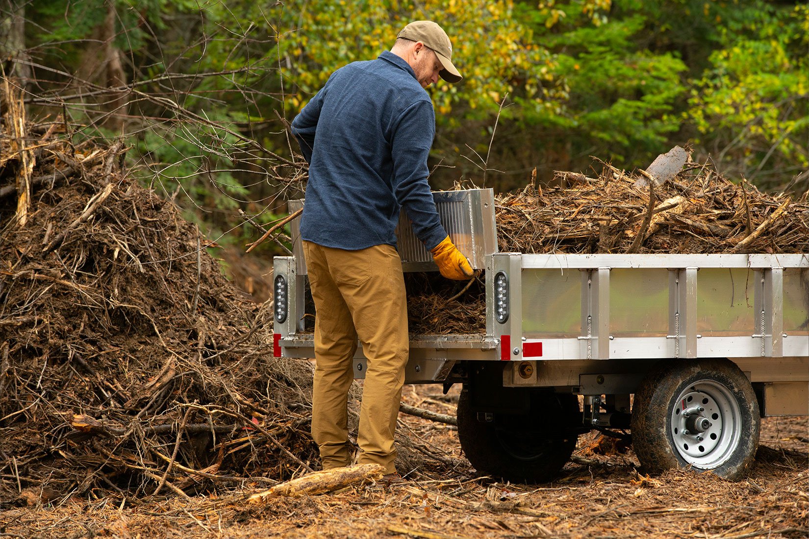 A man using an aluminum homeowner dump trailer to clear away brush during the fall season