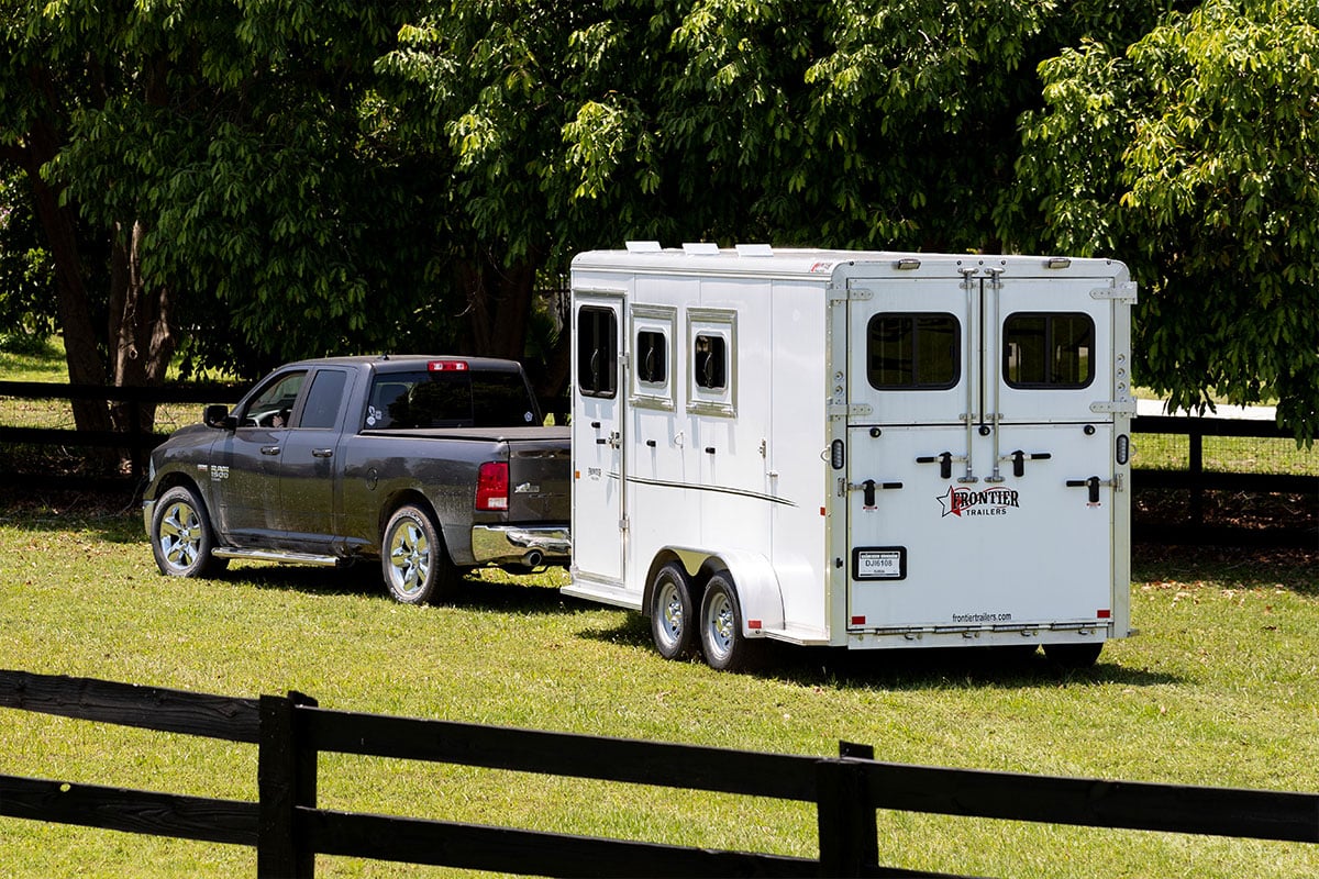 A white aluminum Frontier horse trailer is hitched to a pickup and ready to tow.