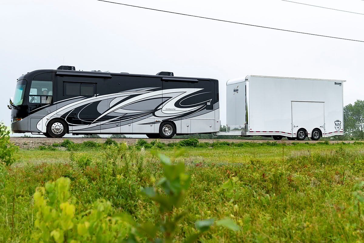 An enclosed aluminum Pinnacle Stacker car hauler by Mission, an ALCOM brand, pulled behind an RV.