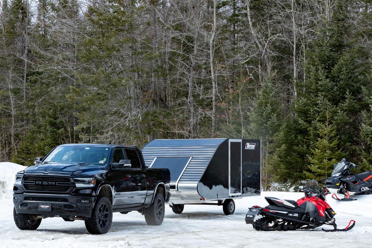 Triton black TC snowmobile trailer, black pickup truck and snowmobile parked on a snowy lot 