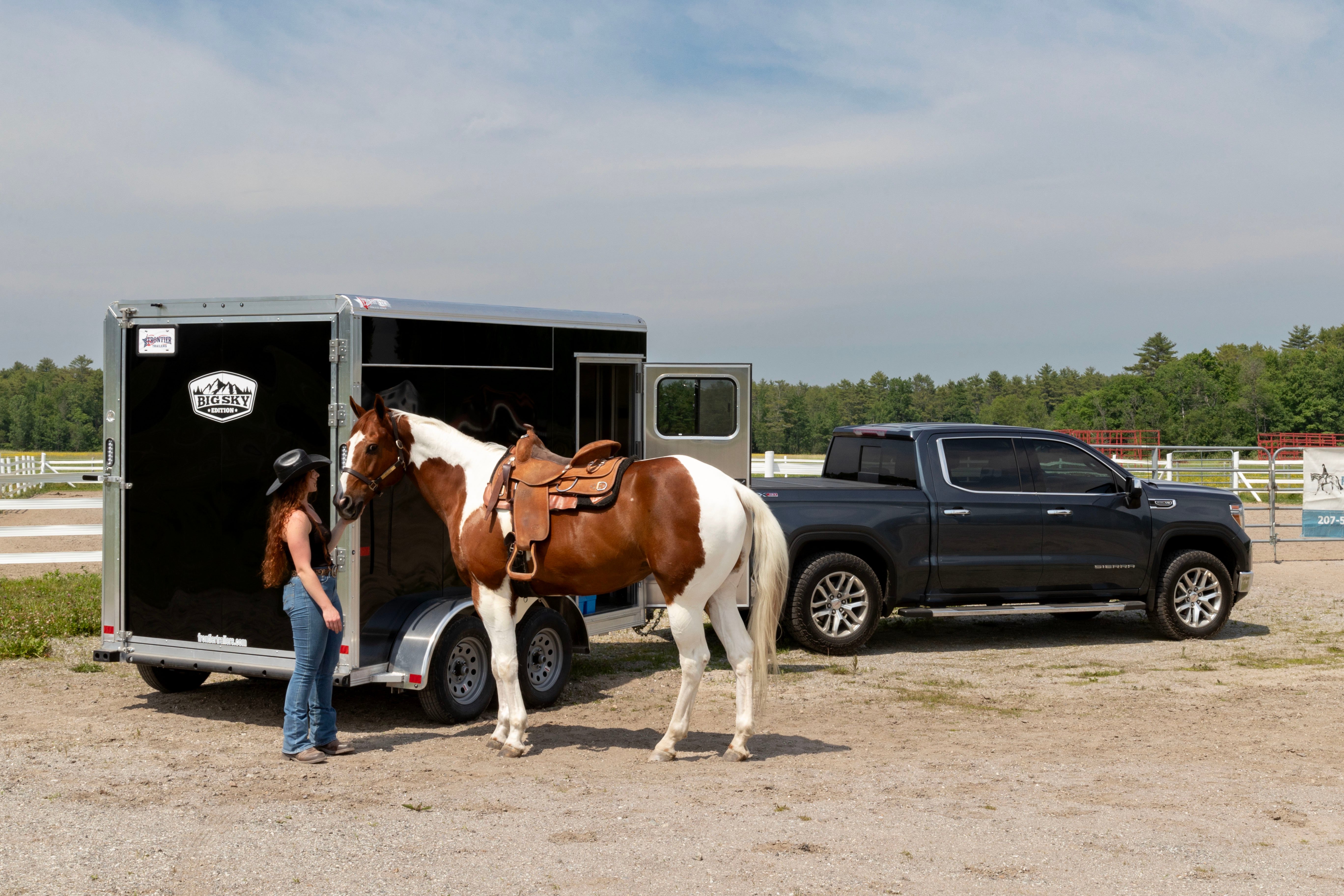 A woman and horse standing beside a black Frontier Trailer hitched to a gray pickup truck