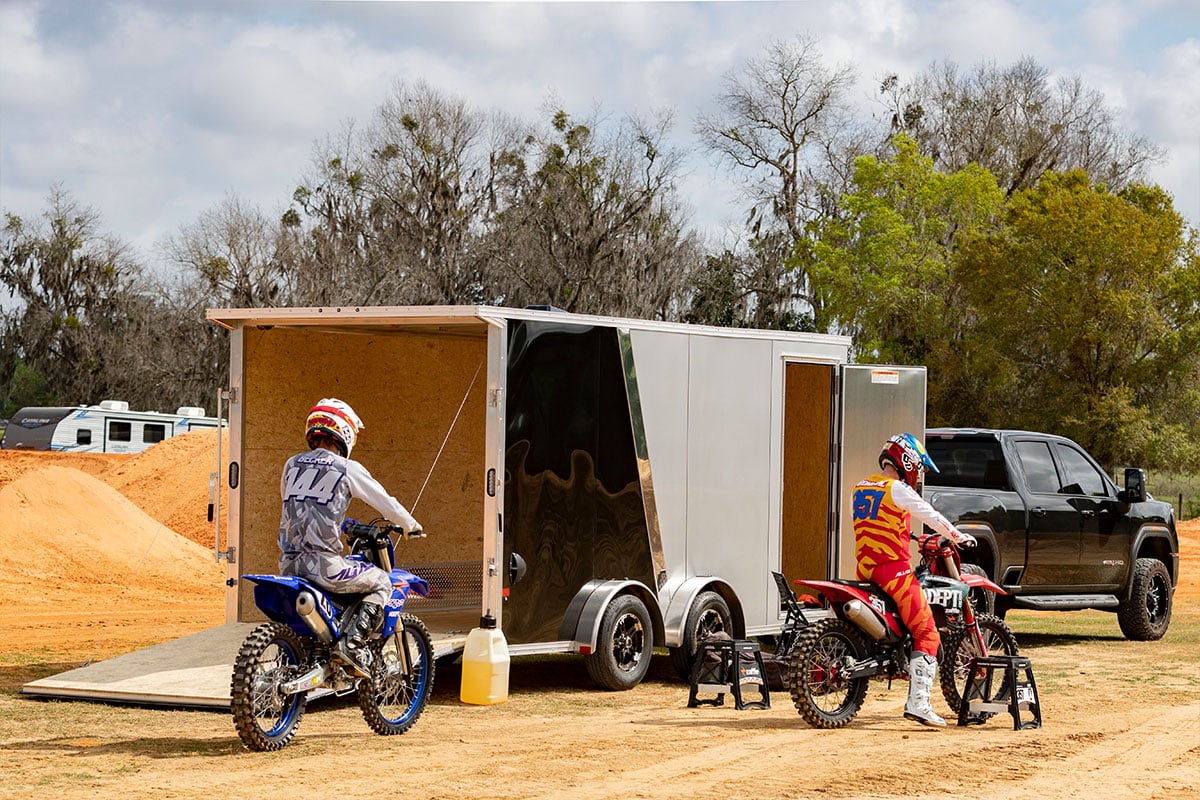 Two dirtbike riders getting ready beside an aluminum motorcycle trailer