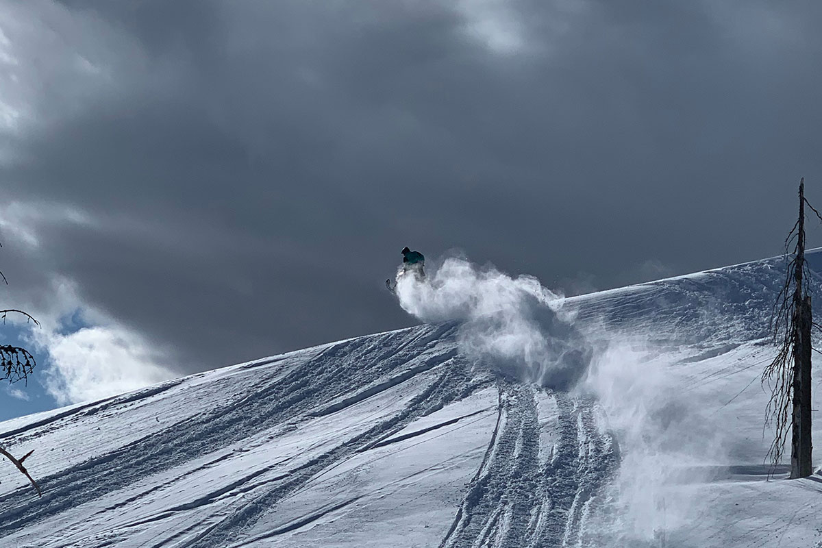 Snowmobiler zooming up a snowy hill in Seeley Lake, MT with a cloudy sky backdrop 