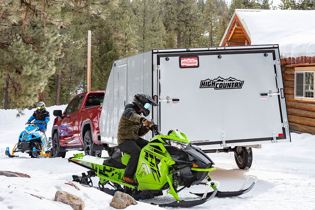 White aluminum crossover snow trailer with two sleds unloaded and ready to ride.