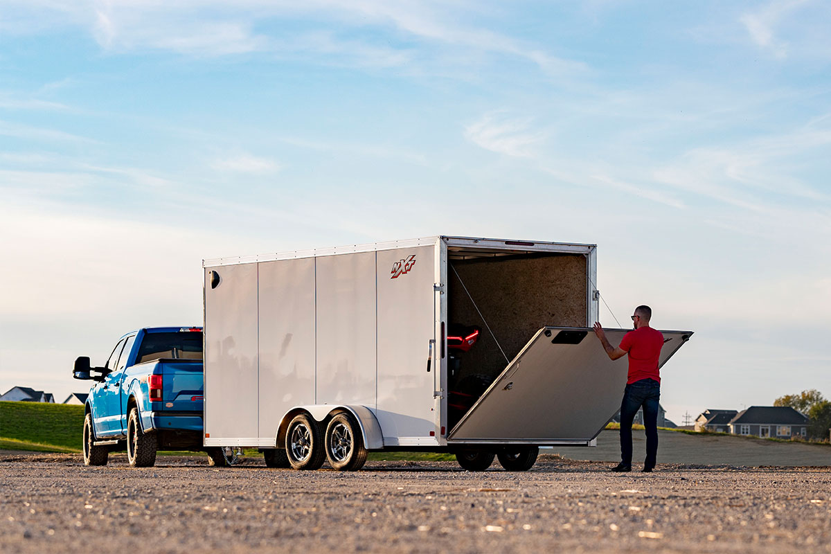 Side view of parked truck with white aluminum cargo trailer; a man is closing the trailer's ramp door.