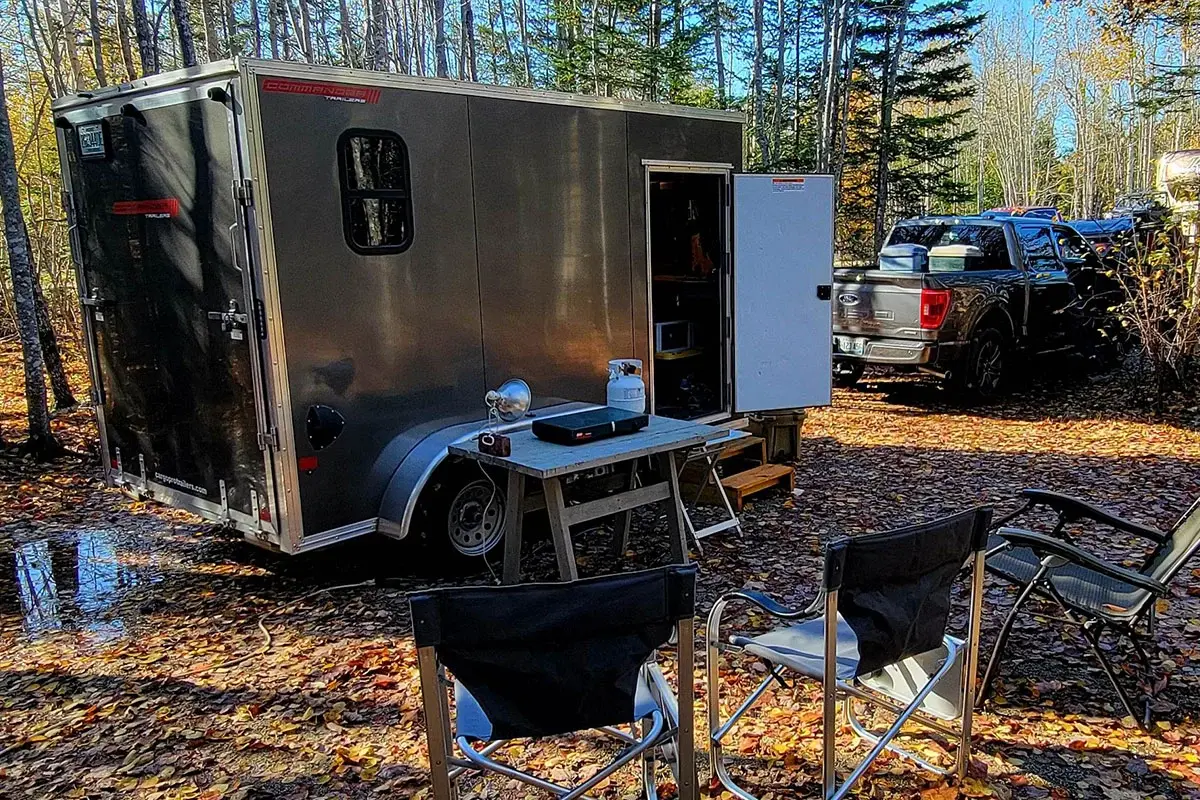ALCOM enclosed aluminum UTV ATV trailer camper parked at a campsite in daylight