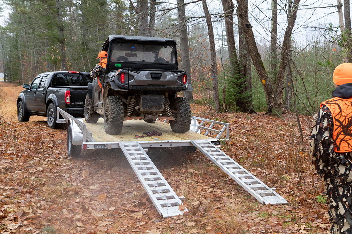 Open ATV trailer by ALCOM with heat treated decking with ATV ready to unload from rear ramps.