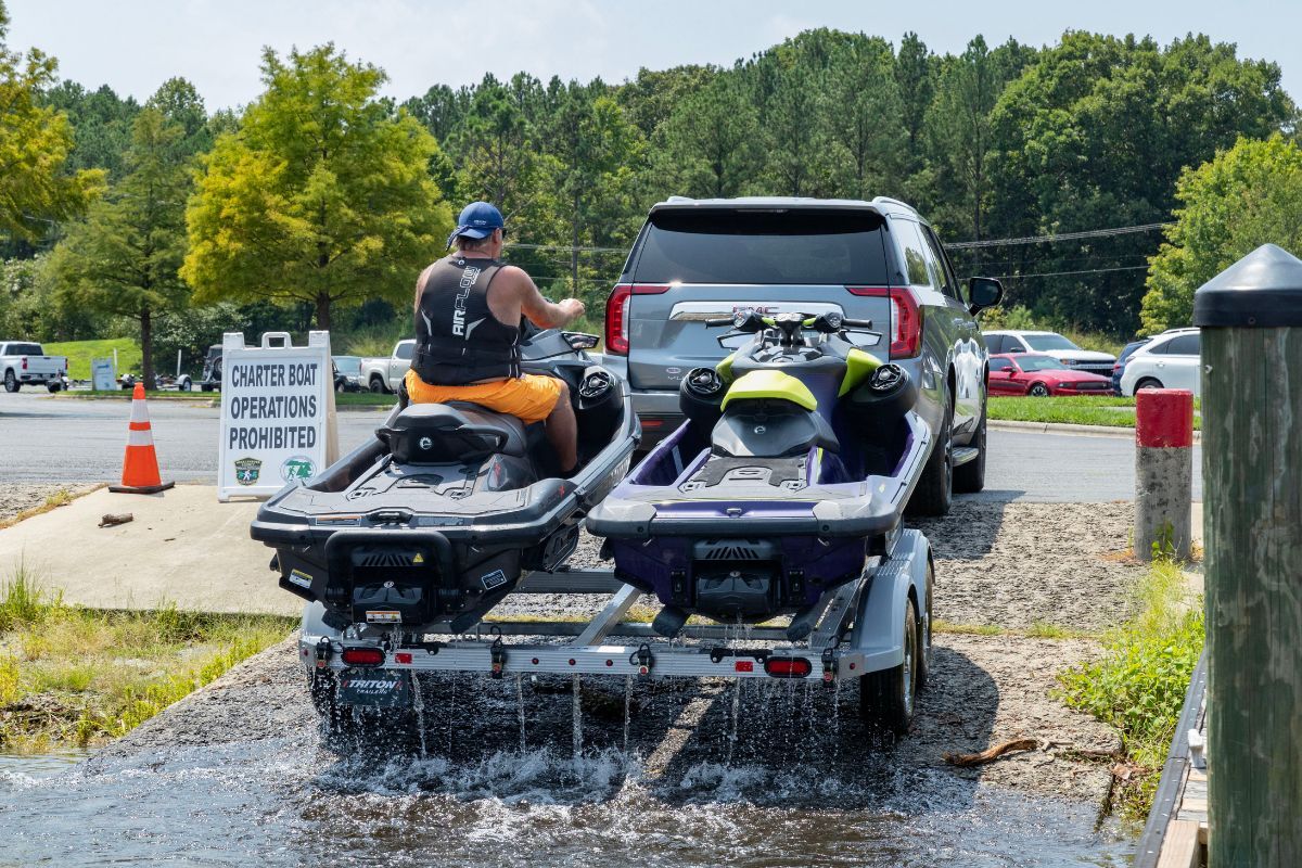 Gray SUV pulling a Triton aluminum PWC trailer up a boat ramp with 2 PWCs and 1 rider