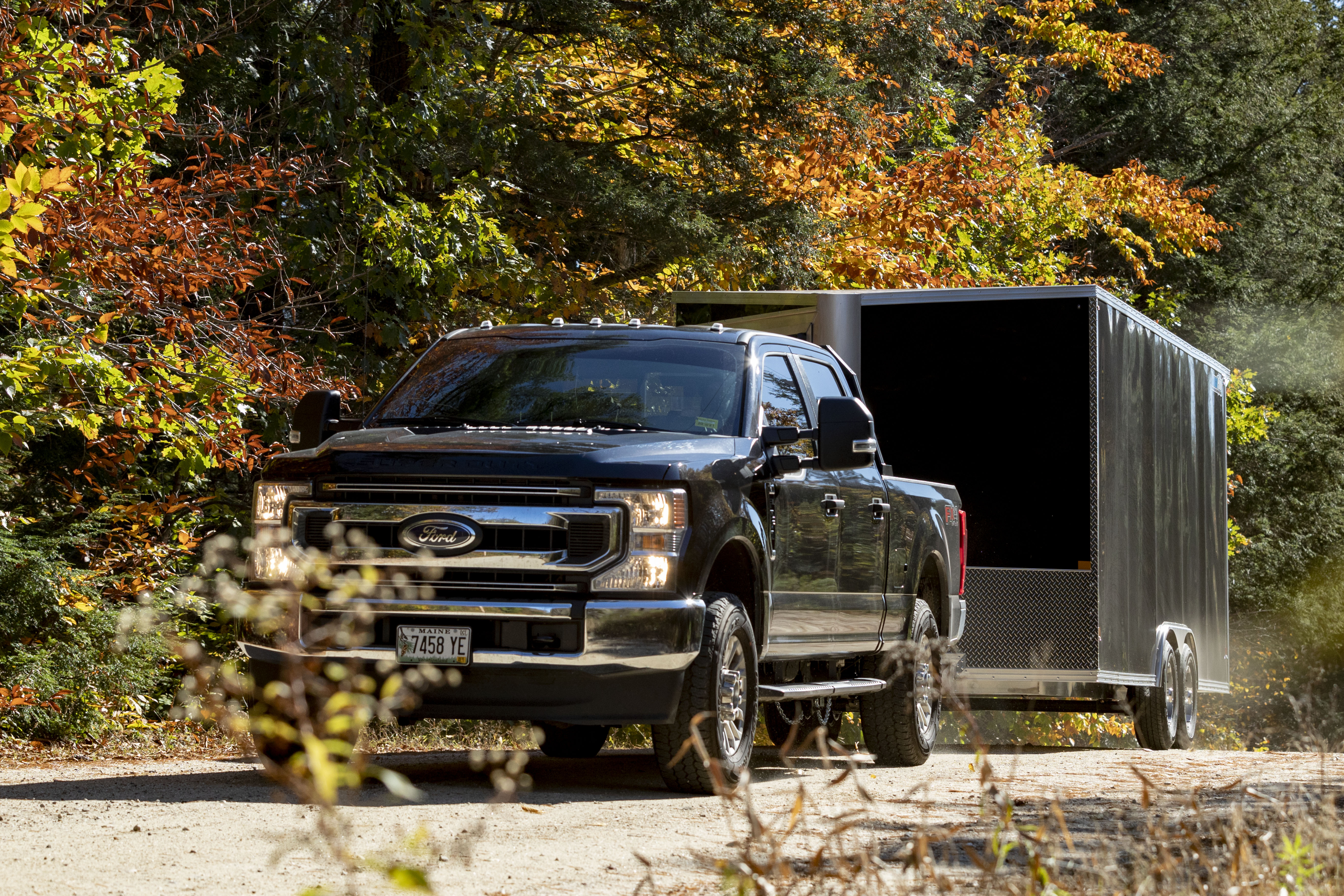 A black pickup truck towing a black CargoPro enclosed aluminum trailer down the road in fall