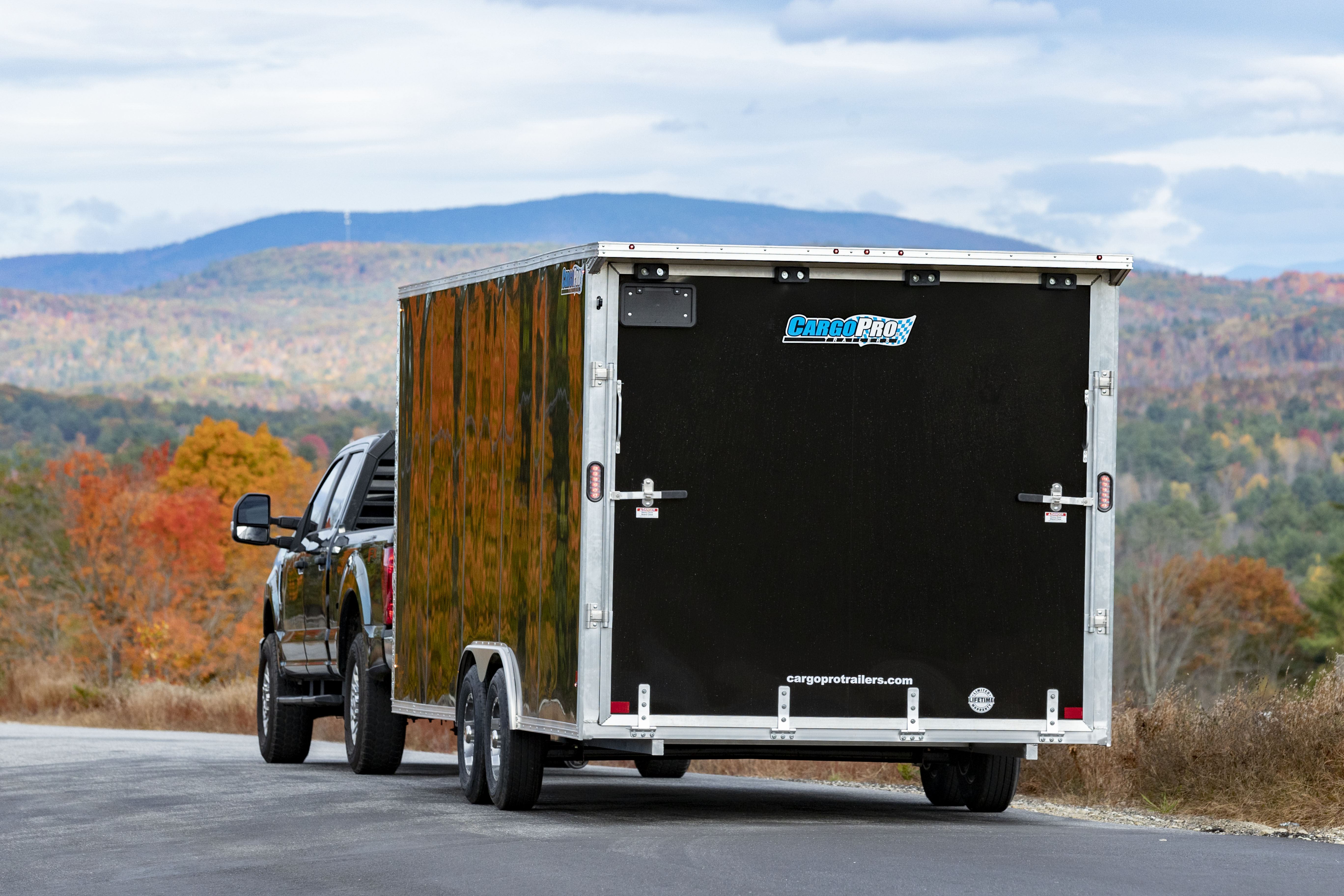 Pickup truck towing a black enclosed aluminum trailer down the road in fall