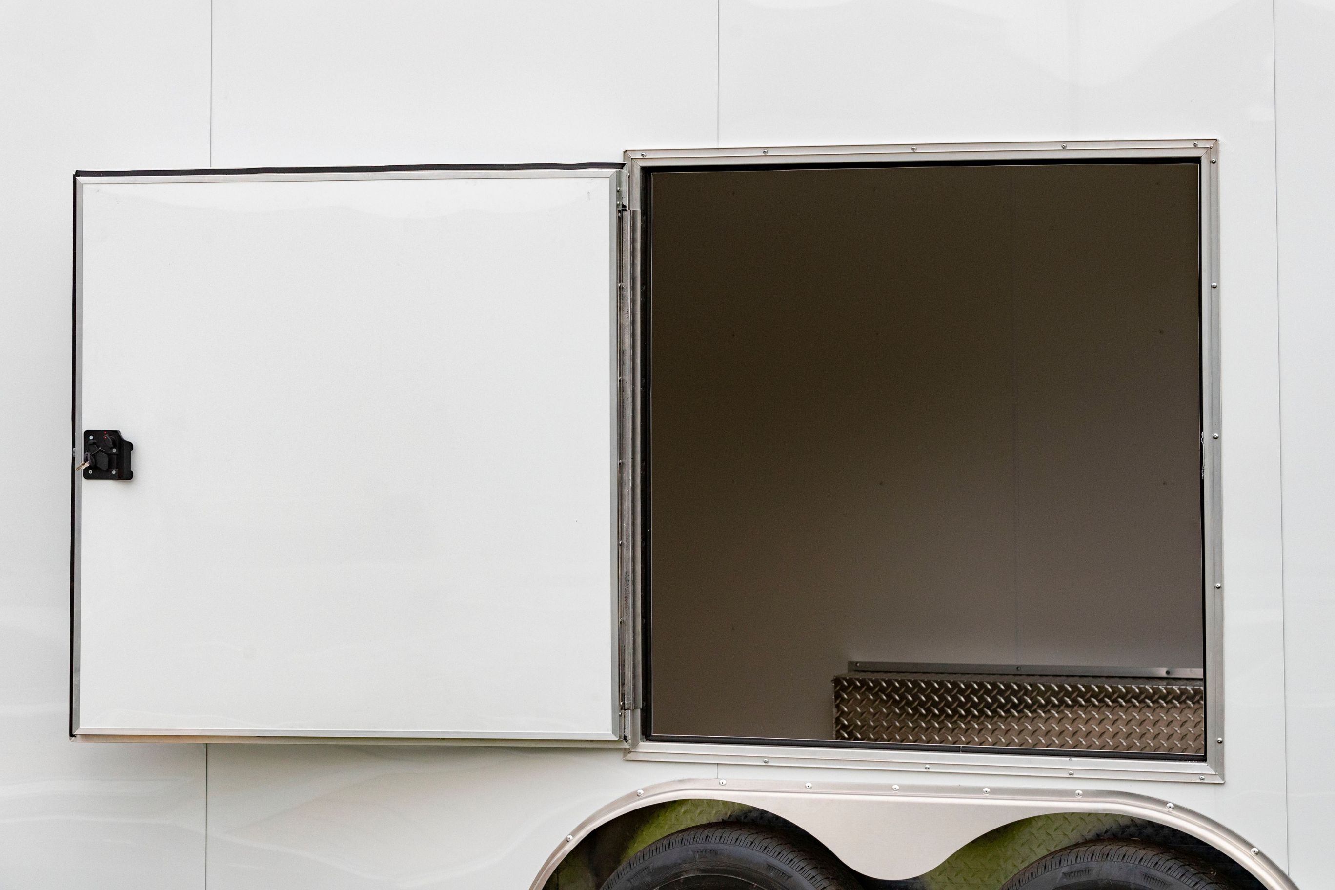 A white tandem axle ALCOM enclosed aluminum cargo trailer with a concession door installed and opened