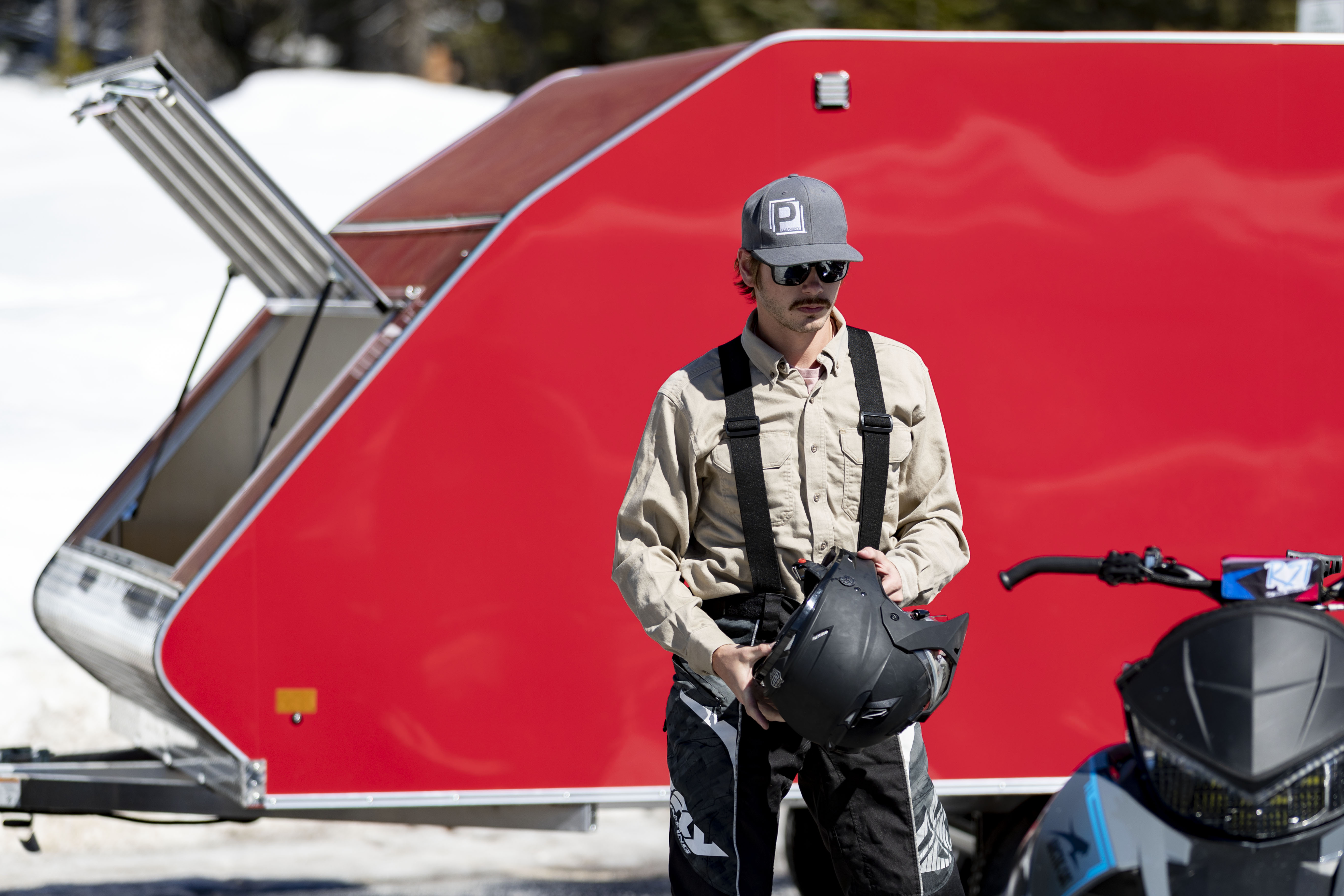 A snowmobiler gets ready to ride in front of a red enclosed Crossover trailer