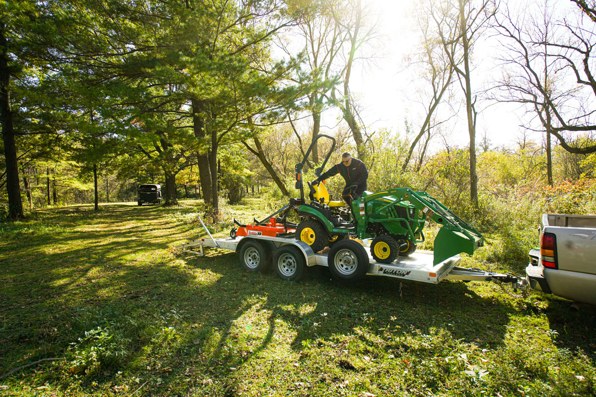 A green tractor loaded onto a heavy-duty open aluminum utility trailer