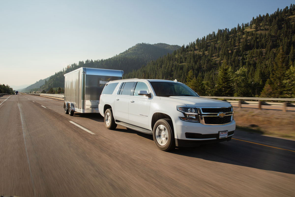 White SUV towing a Pinnacle Series motorcycle trailer down a scenic highway