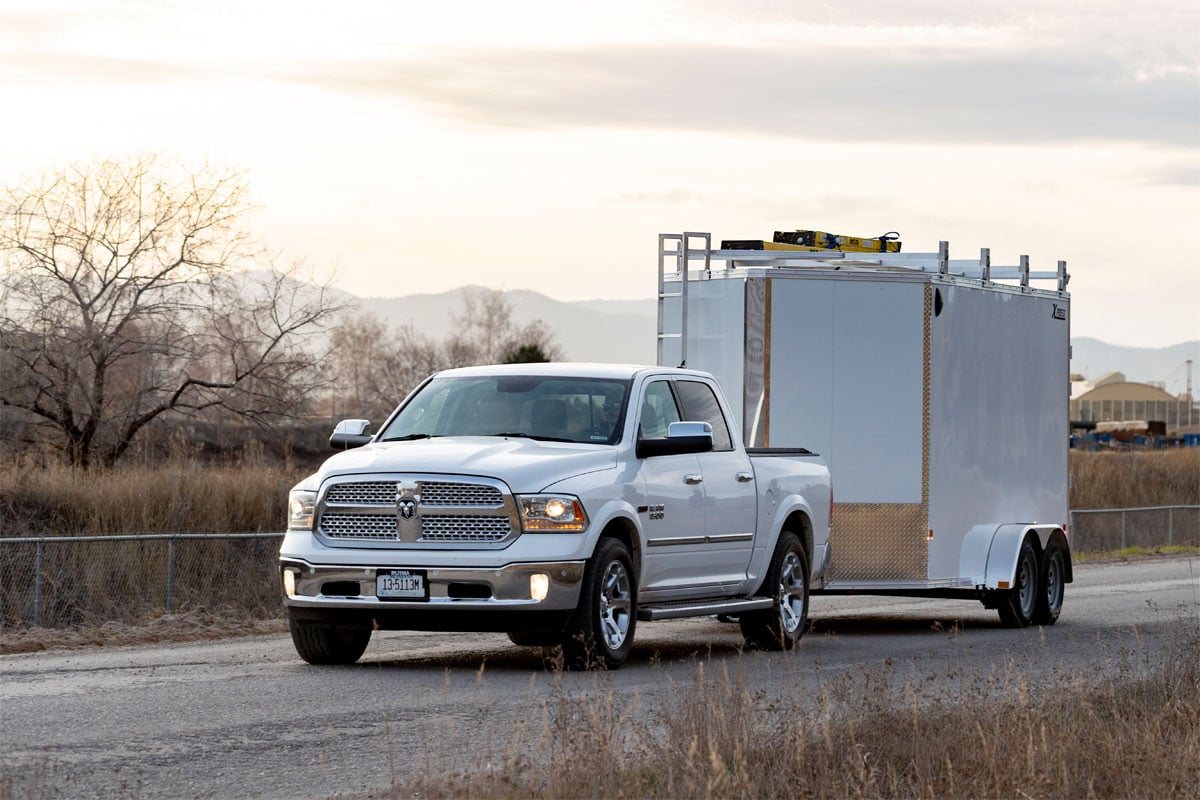 White pickup truck hauling white exterior aluminum contractor trailer with ladder rack, catwalk and stone guard.