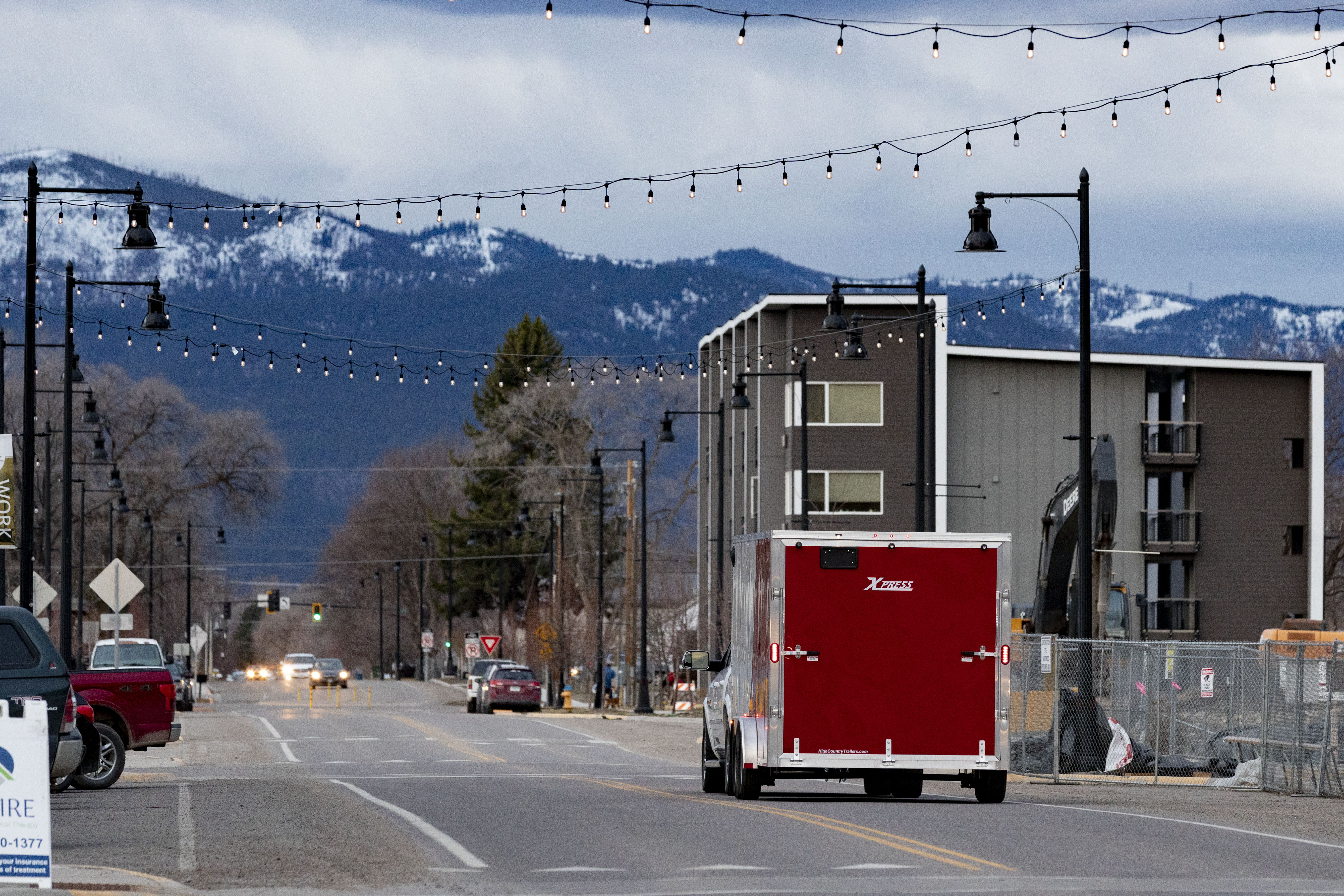 A red ALCOM enclosed cargo trailer towed through a Montana town with mountains in the background