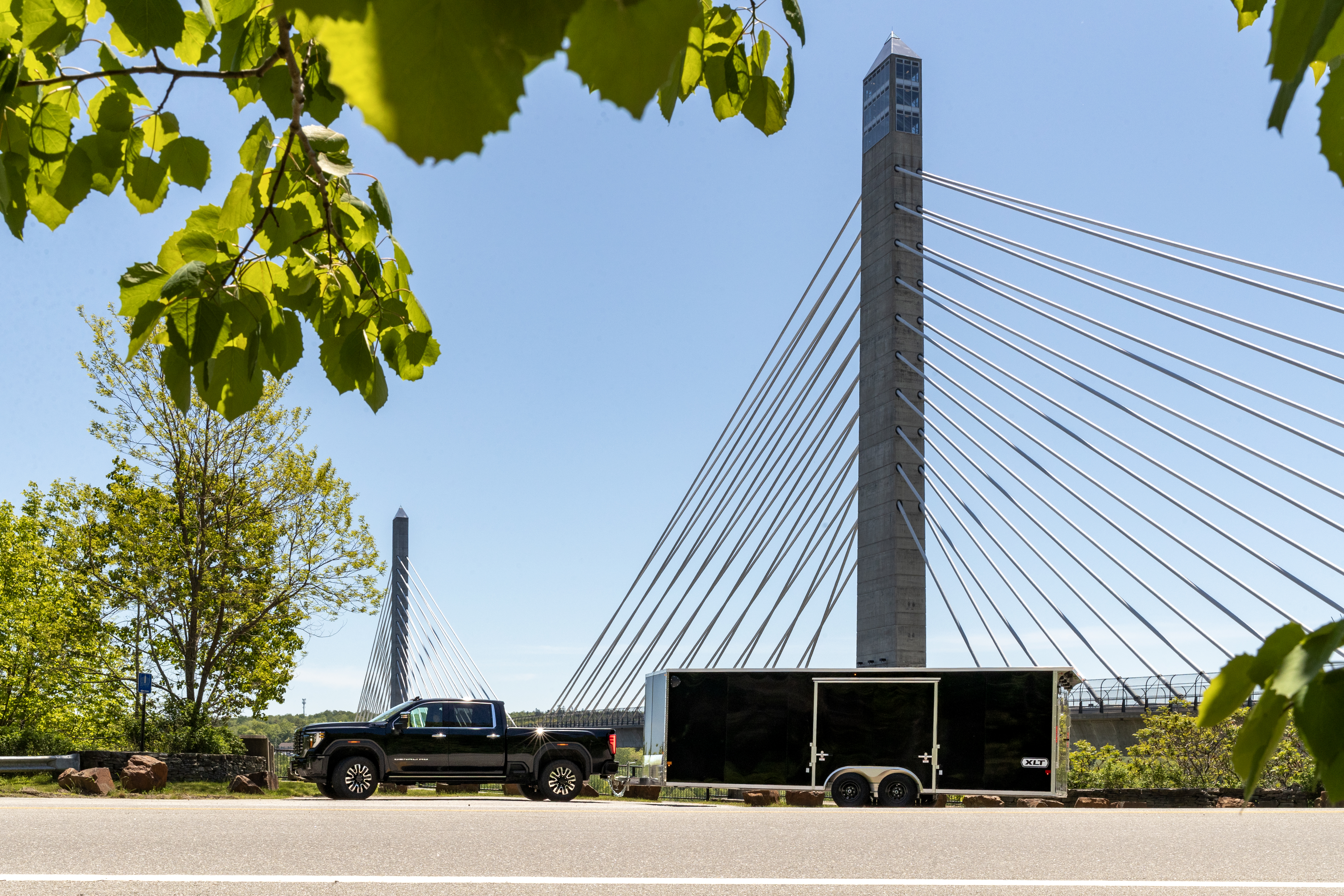 Black pickup and XLT Pro Series car hauler parked in front of a tall bridge in Maine on a sunny summer day