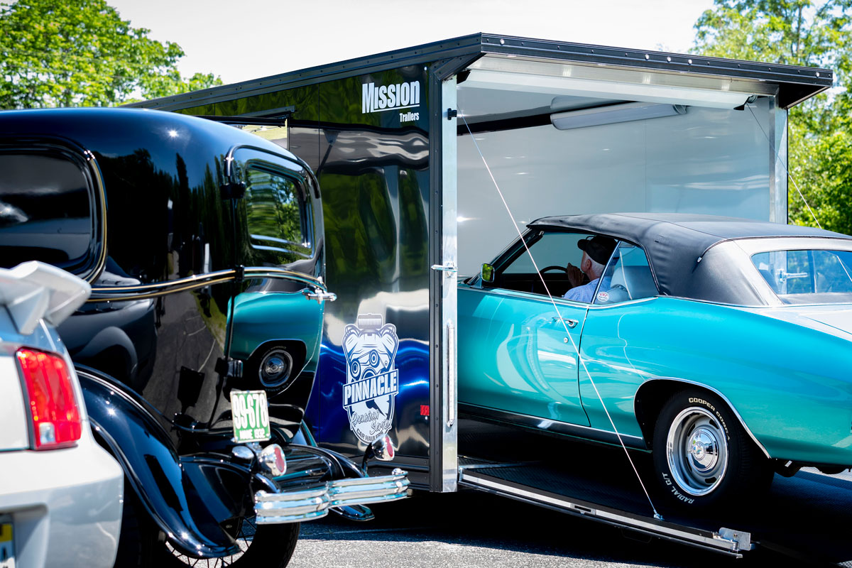 Classic cars and a Mission enclosed Pinnacle Series car hauler parked on a sunny day.