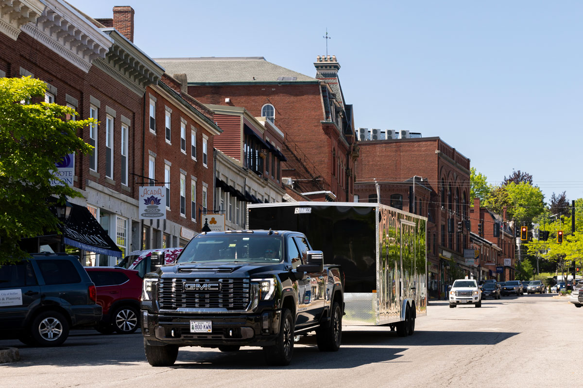 A black pickup tows a sleek black XLT Pro car hauler from ALCOM through a historic downtown on a sunny day