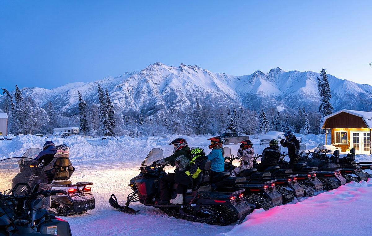 A group of snowmobile riders ready to depart from a snowy cabin 