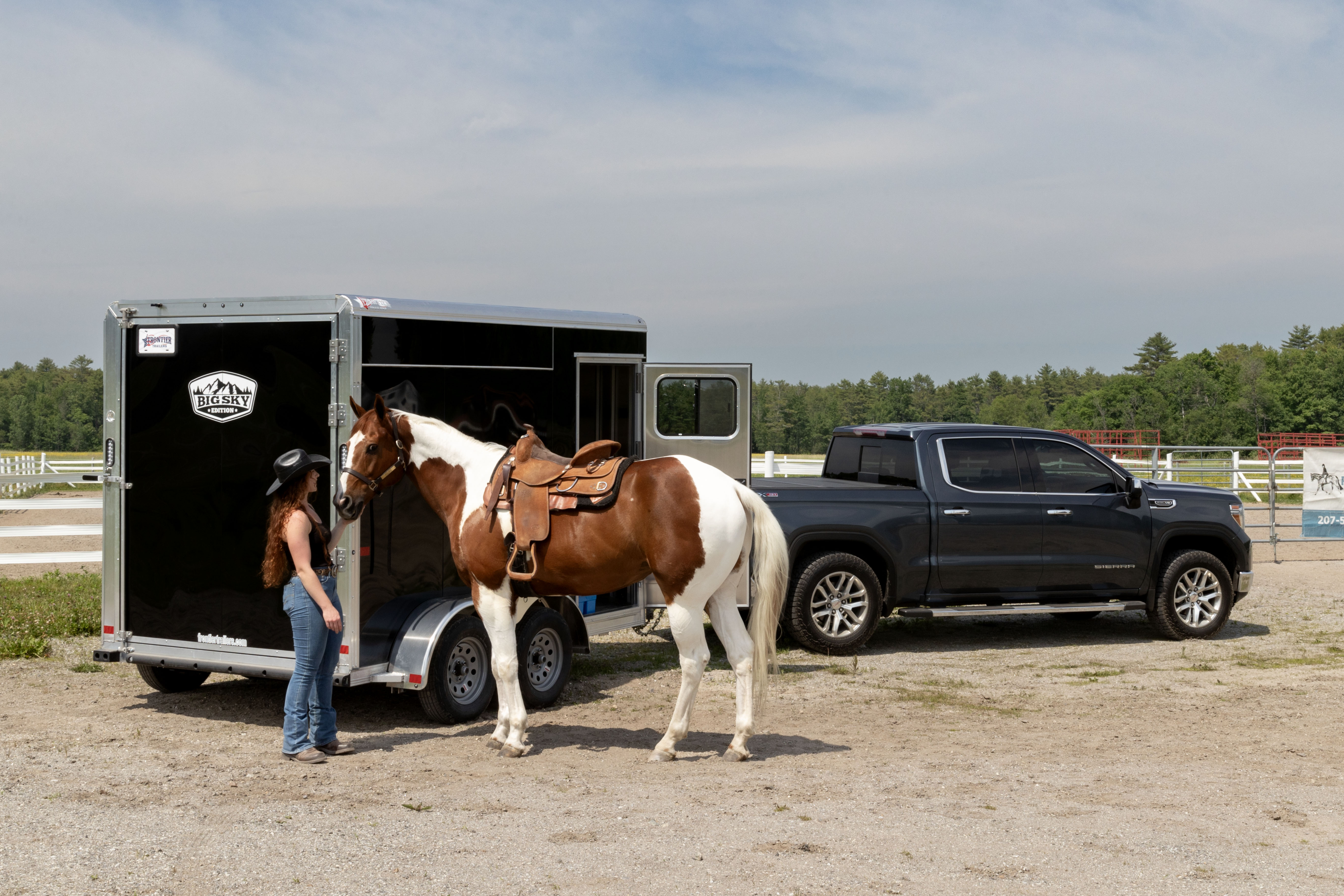 A woman and horse standing beside a black Frontier Trailer hitched to a gray pickup truck