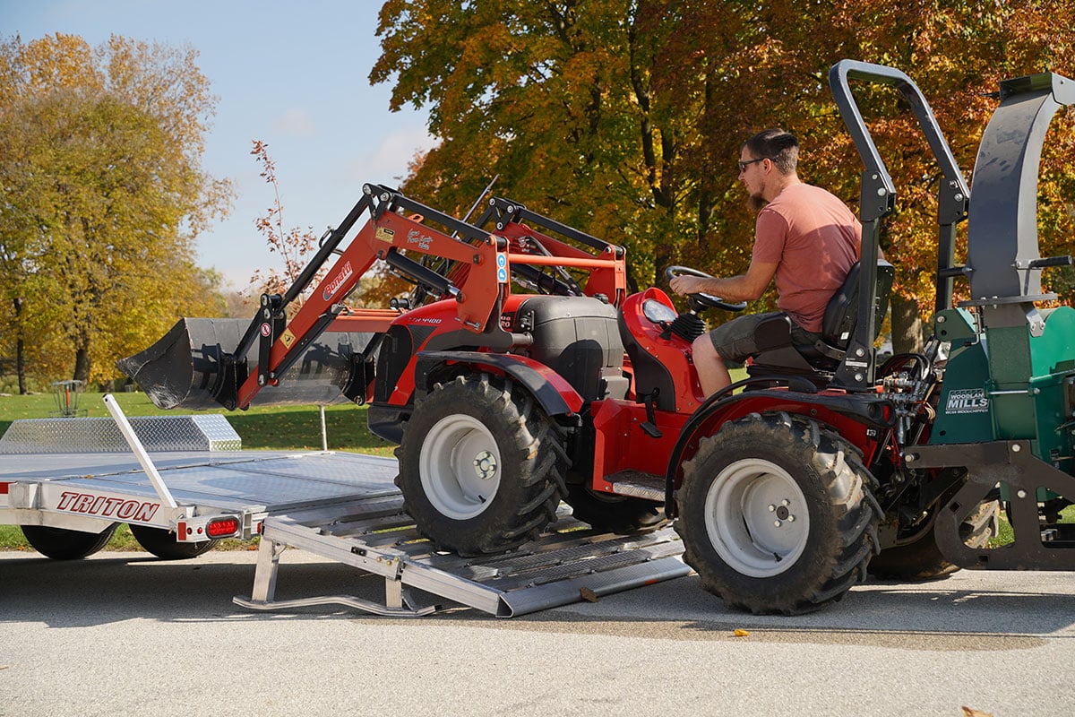 A man loading a tractor onto a Triton aluminum utility trailer 