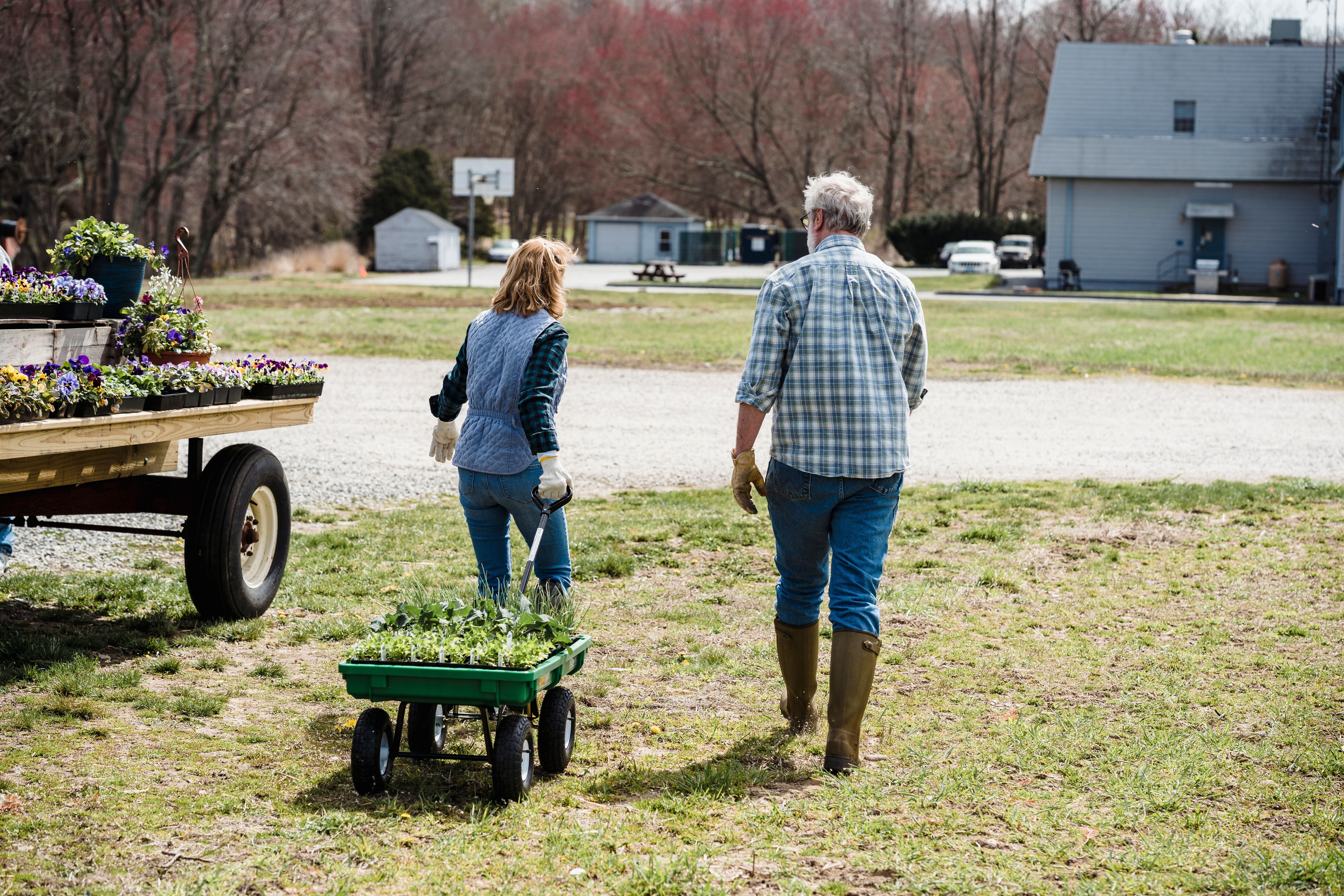 A man and woman in gardening clothes pulling a wagon of plants near a trailer with plants