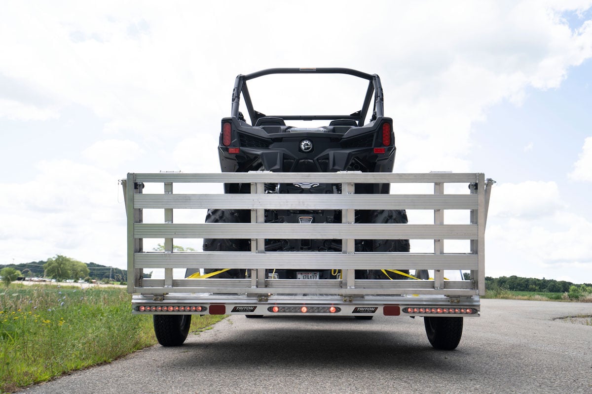 Rear view of an ALCOM aluminum UTV trailer on the road with a bi-fold rear ramp closed up and UTV loaded on the deck